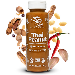 Image of Pretty Thai’s Peanut Dipping and Dressing Sauce. This one has tangy tamarind with a nutty Thai chili twist. Net WT. 10.5 0z (297 g) is also written on it. In the background, some vegetables and nuts can also be seen.