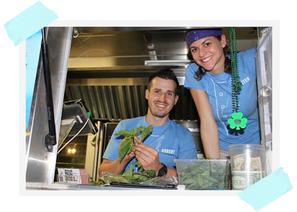 A photo of smiling couple wearing blue t-shirts and man holding green leaves