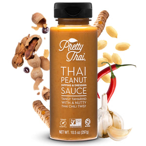 Image of Pretty Thai’s Peanut Dipping and Dressing Sauce. This one has tangy tamarind with a nutty Thai chili twist. Net WT. 10.5 0z (297 g) is also written on it. In the background, some vegetables and nuts can also be seen.