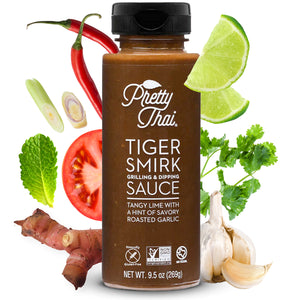 A bottle of Pretty Thai Tiger smirk grilling and dripping sauce, which has tangy lime with a hint of savory roasted garlic. Net WT. 9.5 0z (269 g) is also written on it under different labels. In the background, different vegetables can be seen.