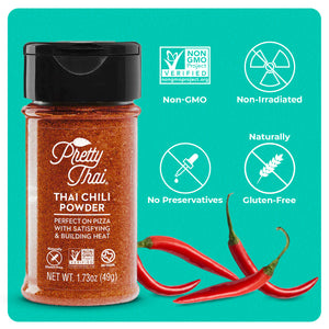 A bottle of Pretty Thai’s Thai Chili Powder. which will be perfect on pizza with satisfying and building heat. Net WT. 1.73 oz (49 g) is also written on it under different labels. In the background, red chilis can be seen.