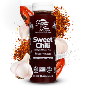 A bottle of Pretty Thai Sweet Chili Stir Fry and Barbecue Sauce, which has savory garlic with sweet caramelization. Net WT. 11.20z (317 g) is also written on it under the different labels. In the background mixture of red chilis and garlic pieces can be seen. 