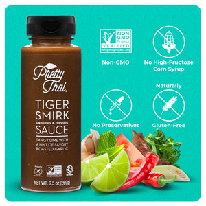 A bottle of Pretty Thai Tiger smirk grilling and dripping sauce, which has tangy lime with a hint of savory roasted garlic. Net WT. 9.5 0z (269 g) is also written on it under different labels. In the bottom right corner, different vegetables can be seen. four white icons are present. These icons read “Non-GMO, No High-Fructose Corn Syrup, No Preservatives, and Naturally Gluten-Free”.