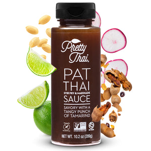 A bottle of Pretty Thai PAT Thai Stir Fry and Marinade Sauce, which hasIt has savory with a tangy punch of tamarind. Net WT. 10.2 0z (289 g) is also written on it under different labels. In the background, different nuts and vegetables can be seen. 