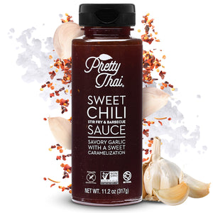 A bottle of Pretty Thai Sweet Chili Stir Fry and Barbecue Sauce, which has savory garlic with sweet caramelization. Net WT. 11.20z (317 g) is also written on it under the different labels. In the background mixture of red chilis and garlic pieces can be seen. 